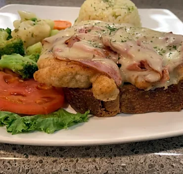 Open-faced chicken cordon bleu with tomato slices and vegetables