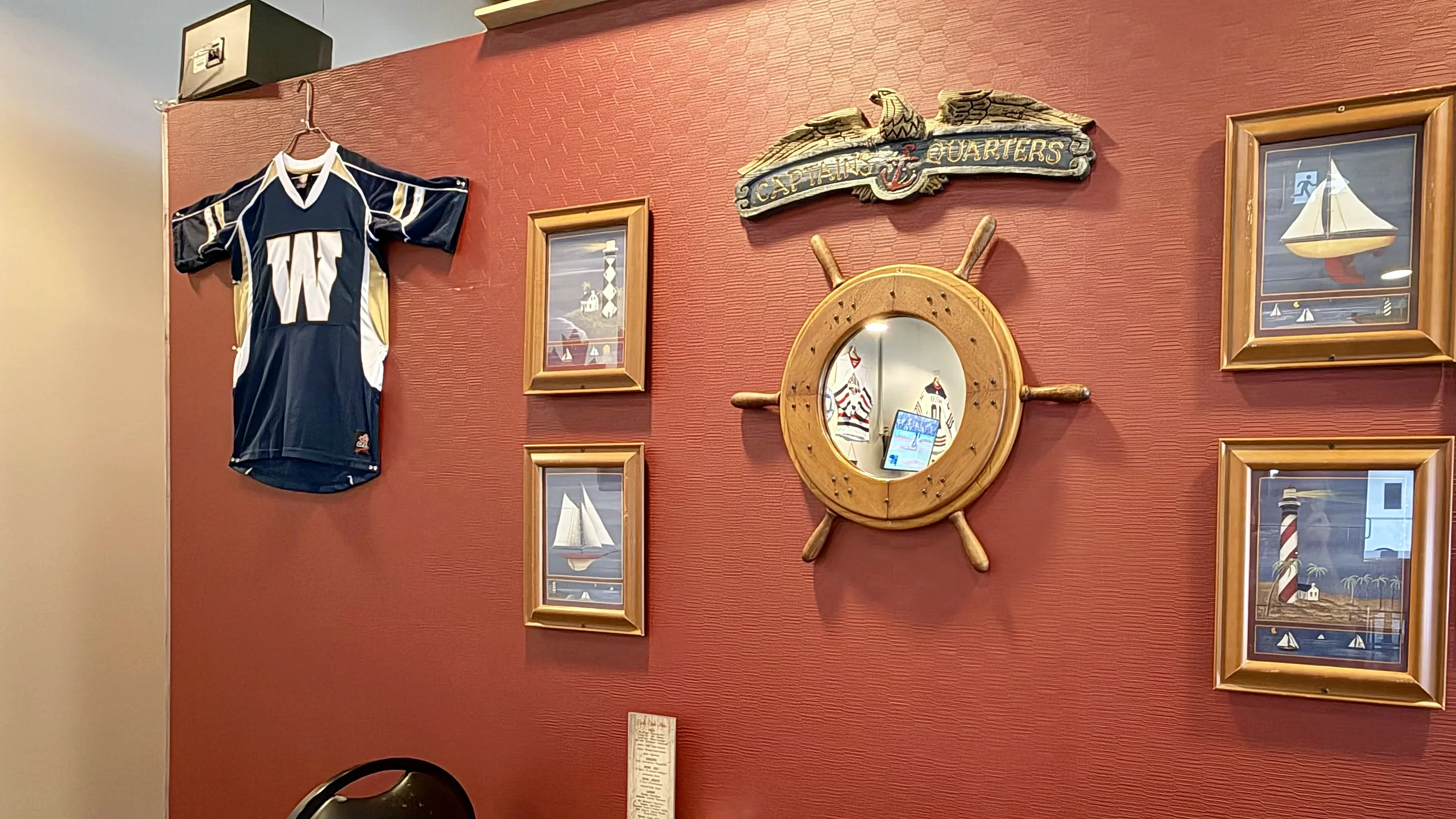 Riverboat dining room wall with a ship's wheel, sailboat pictures and a football jersey